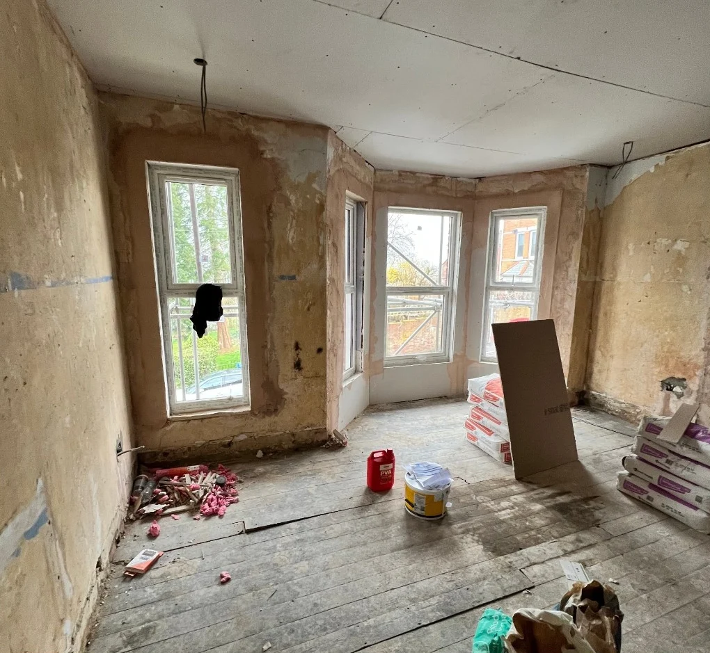 Bay-window room stripped to bare walls and floorboards